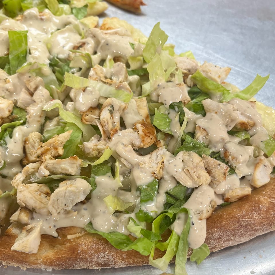 Close-up of a Sofia Pizza chicken Caesar salad pizza with dressing, lettuce, and chicken.