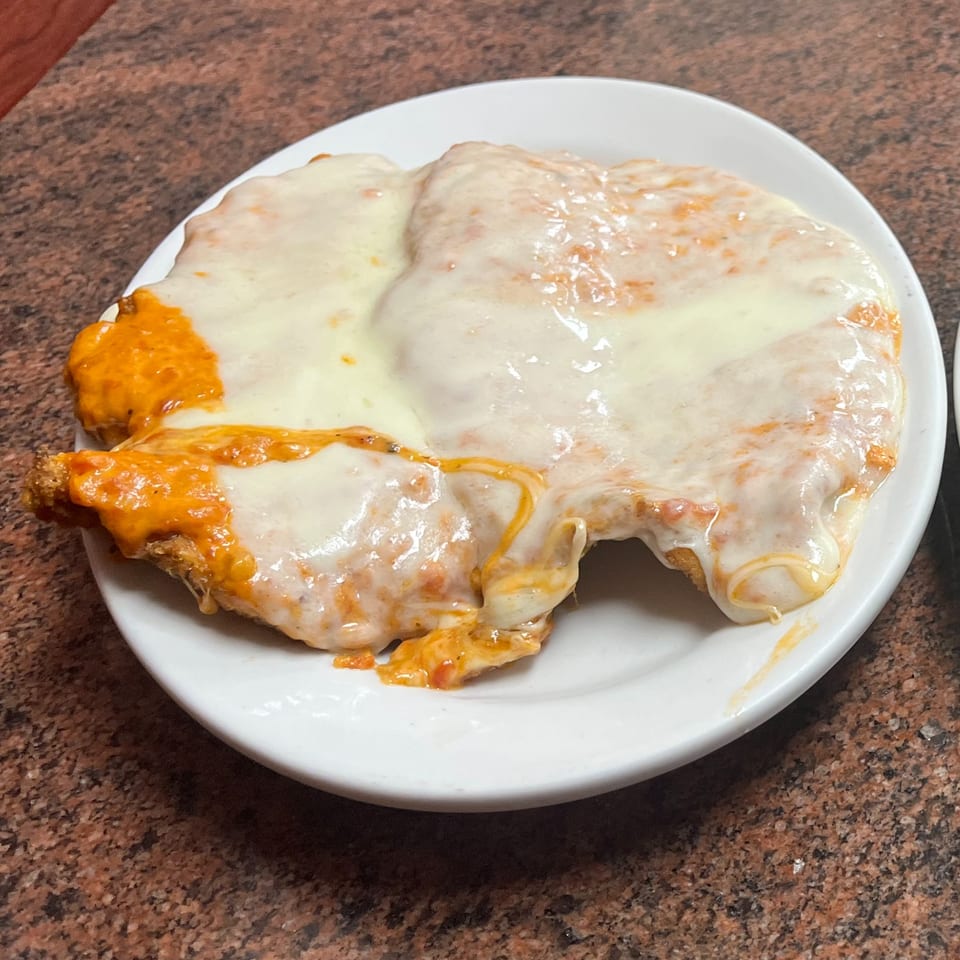 A chicken parmesan dish from Sofia Pizza, covered in melted mozzarella and marinara sauce on a white plate.