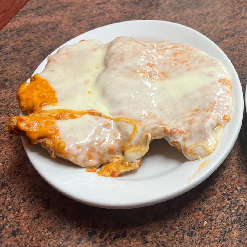 A chicken parmesan dish from Sofia Pizza, covered in melted mozzarella and marinara sauce on a white plate.