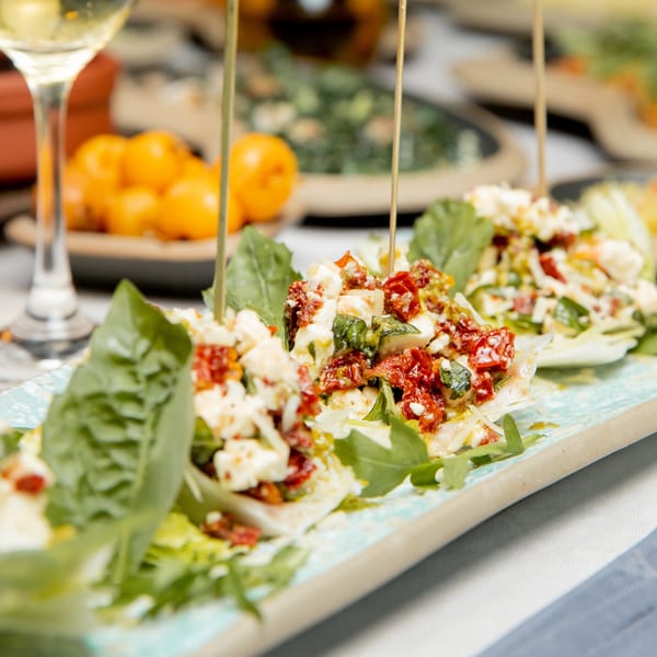 Close-up of Italian appetizers with sun-dried tomatoes, feta, and greens on a light blue platter.