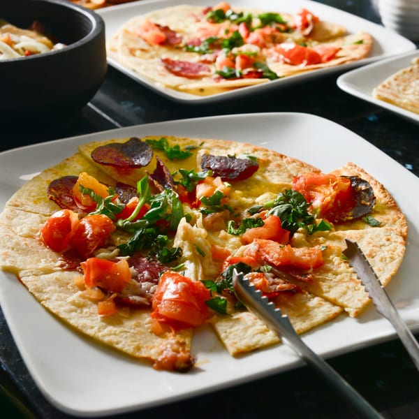 Several Sofia Pizza flatbreads with tomatoes, greens, and pepperoni on white plates.