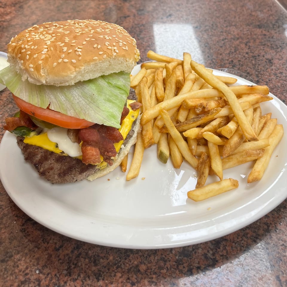 A bacon cheeseburger with lettuce and tomato, served with a side of golden french fries.