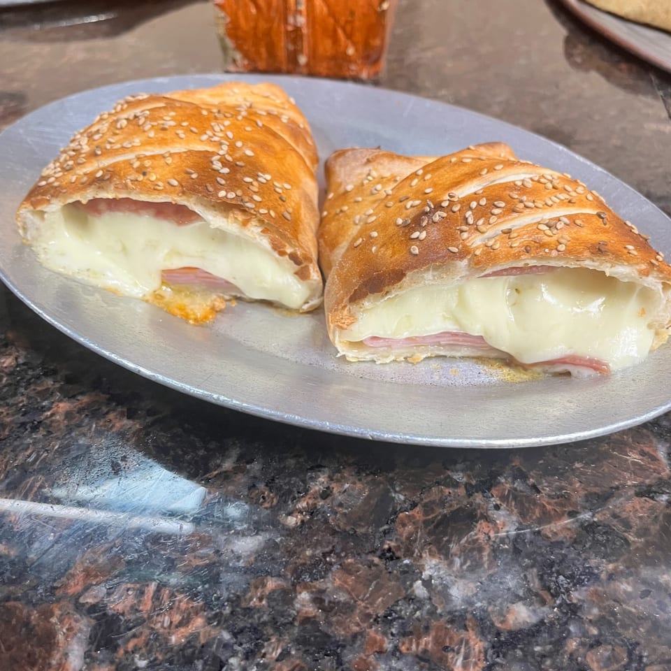Two golden-brown calzones, filled with melted cheese and ham, on a silver plate.