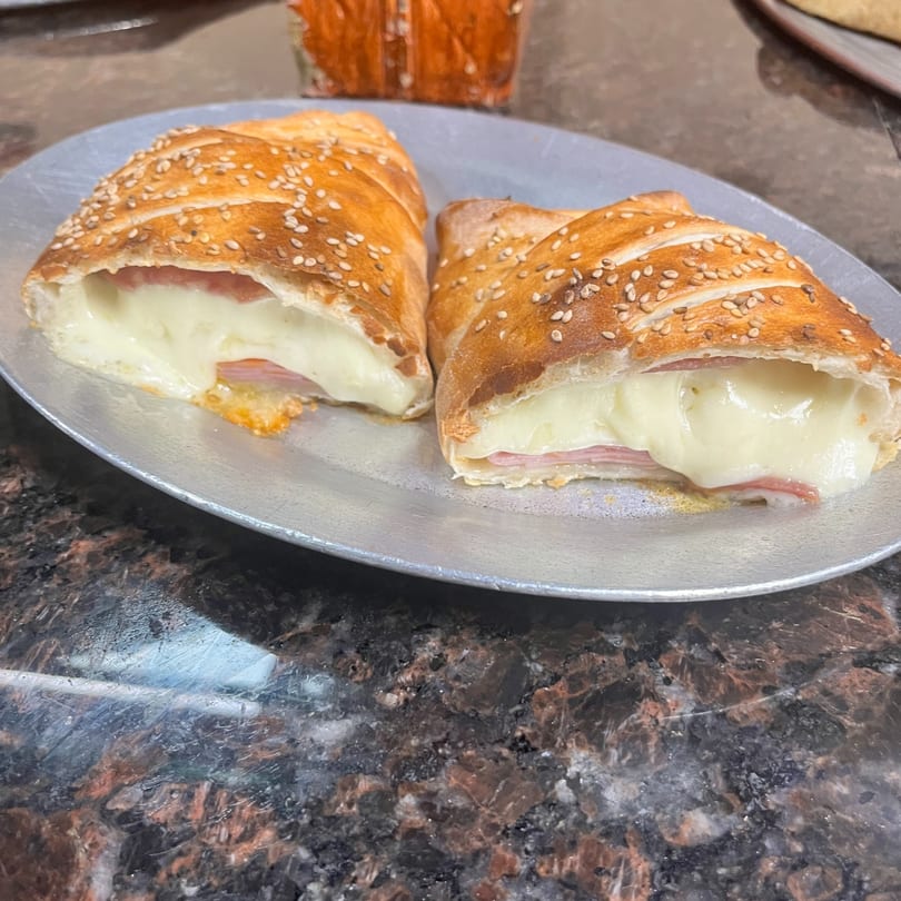 Two golden-brown calzones, filled with melted cheese and ham, on a silver plate.